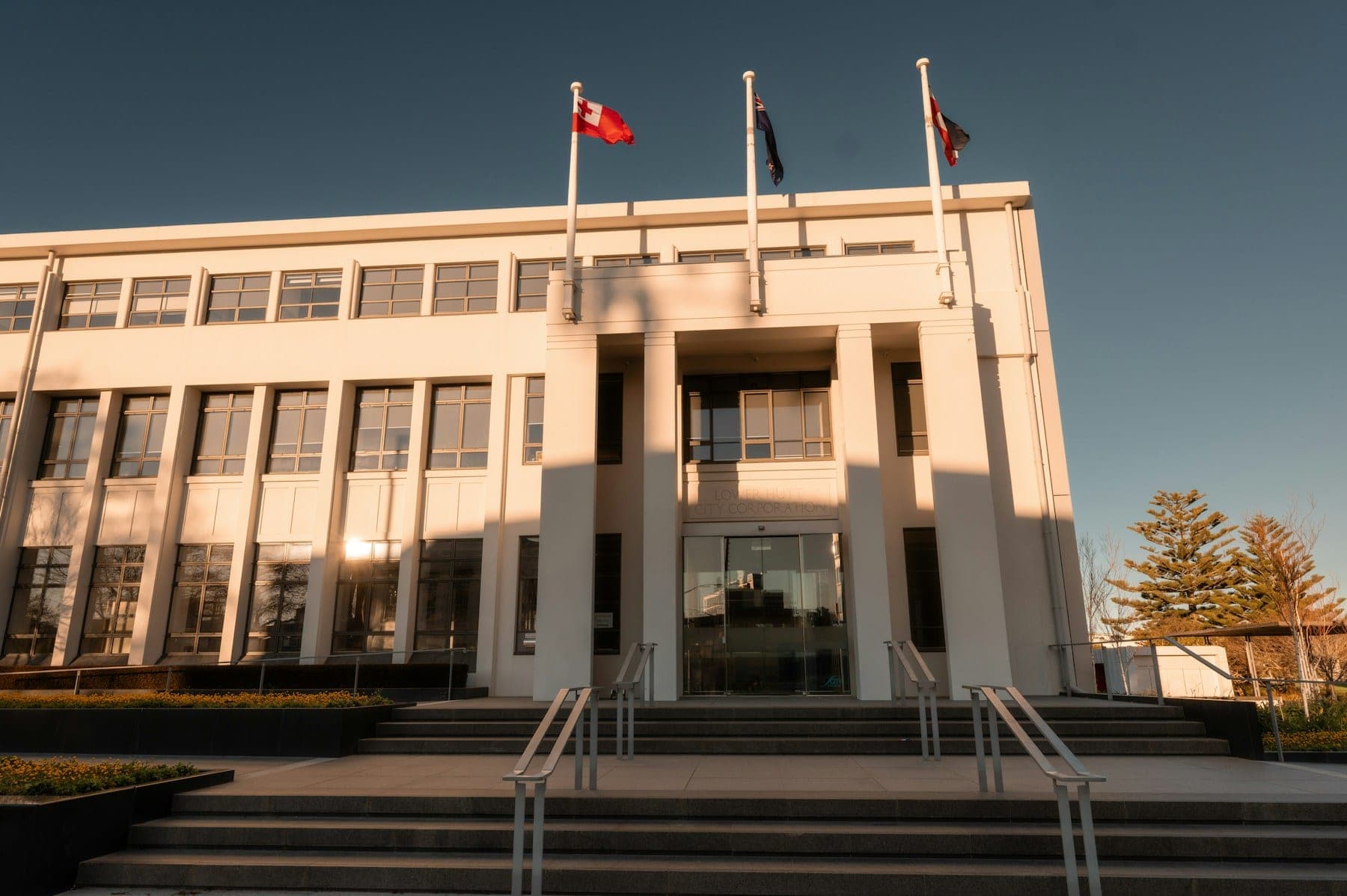 The entrance of a modern civic building, with flags flying under a clear sky.