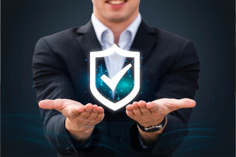 A man in a suit holding out both hands beneath a glowing shield-and-checkmark graphic.