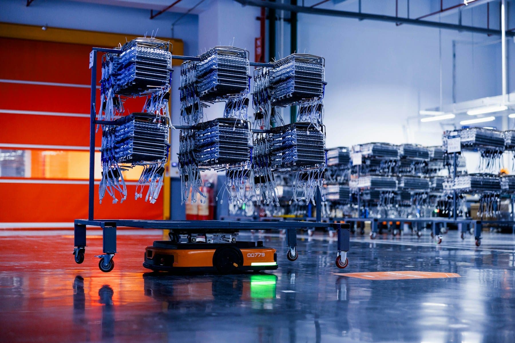 An automated guided vehicle carrying a loaded parts rack across a warehouse floor.