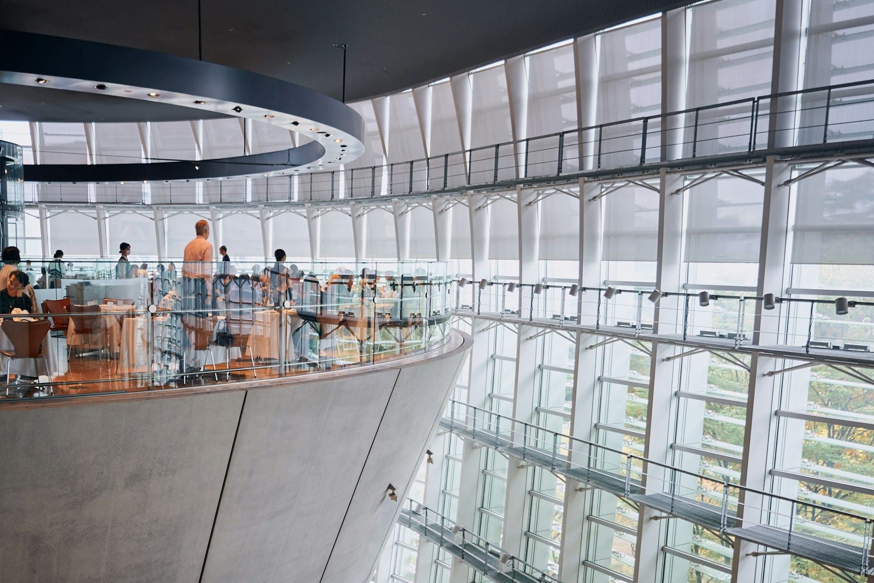 People on the curved balconies of a warm, open office atrium, looking out over the floors below.