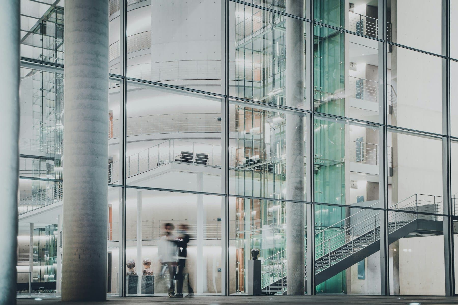A glass-walled office atrium with people moving between its upper floors.
