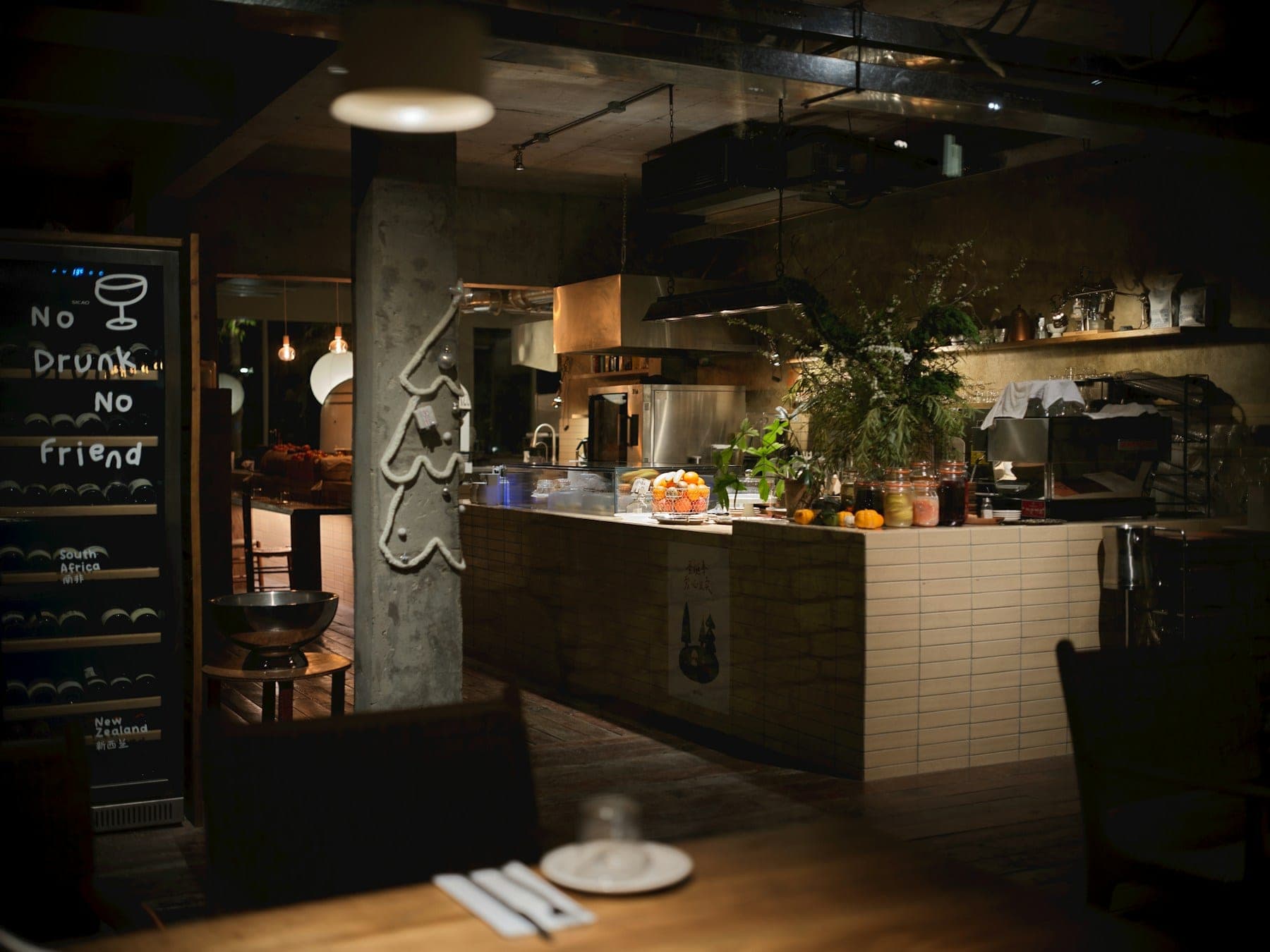 An open restaurant kitchen seen from the dining room, with herb planters and a chalkboard alongside it
