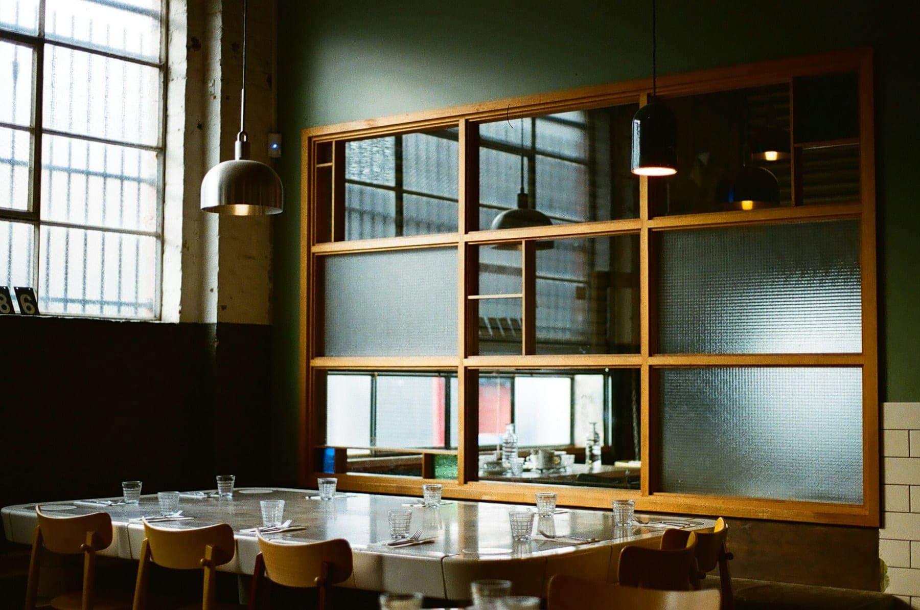 A restaurant dining room with a deep green wall, timber-framed windows, and a long table laid for service