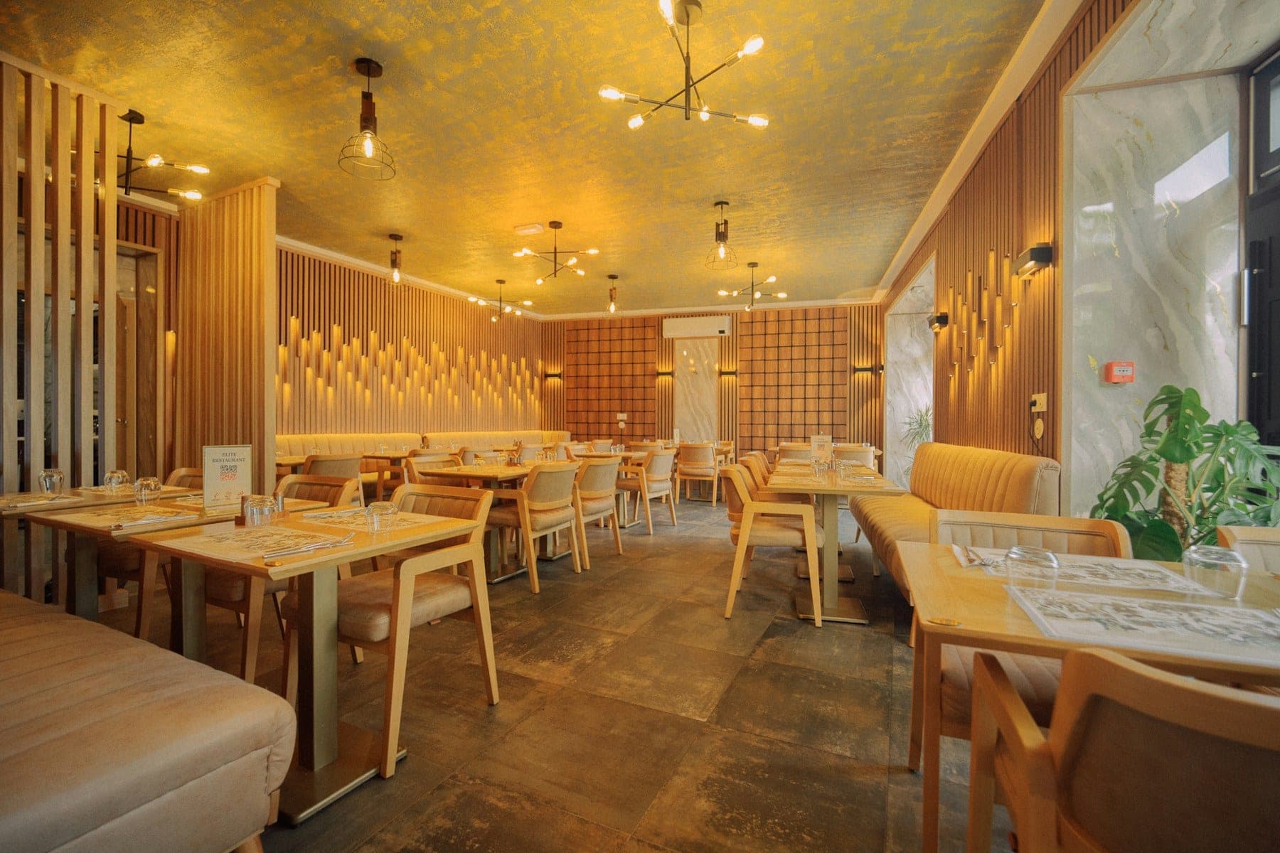 The dining room of a full-service restaurant, with wood-slat walls and a warm gold ceiling