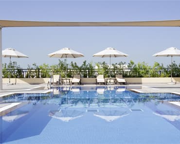 A terrace swimming pool lined with white parasols and sun loungers under a clear sky.