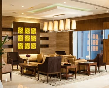 A hotel lobby lounge with sofas and armchairs around low tables, under a row of pendant lamps.