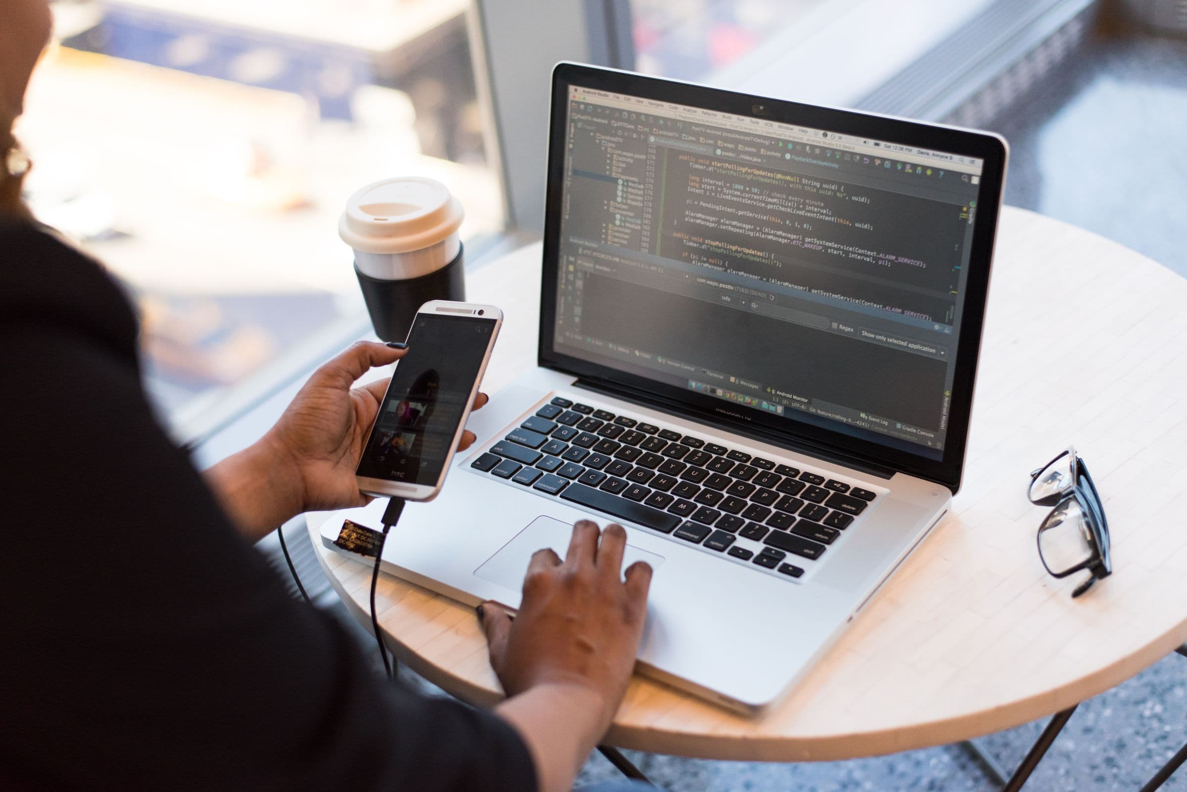 Developer testing a mobile app on a smartphone connected to a laptop